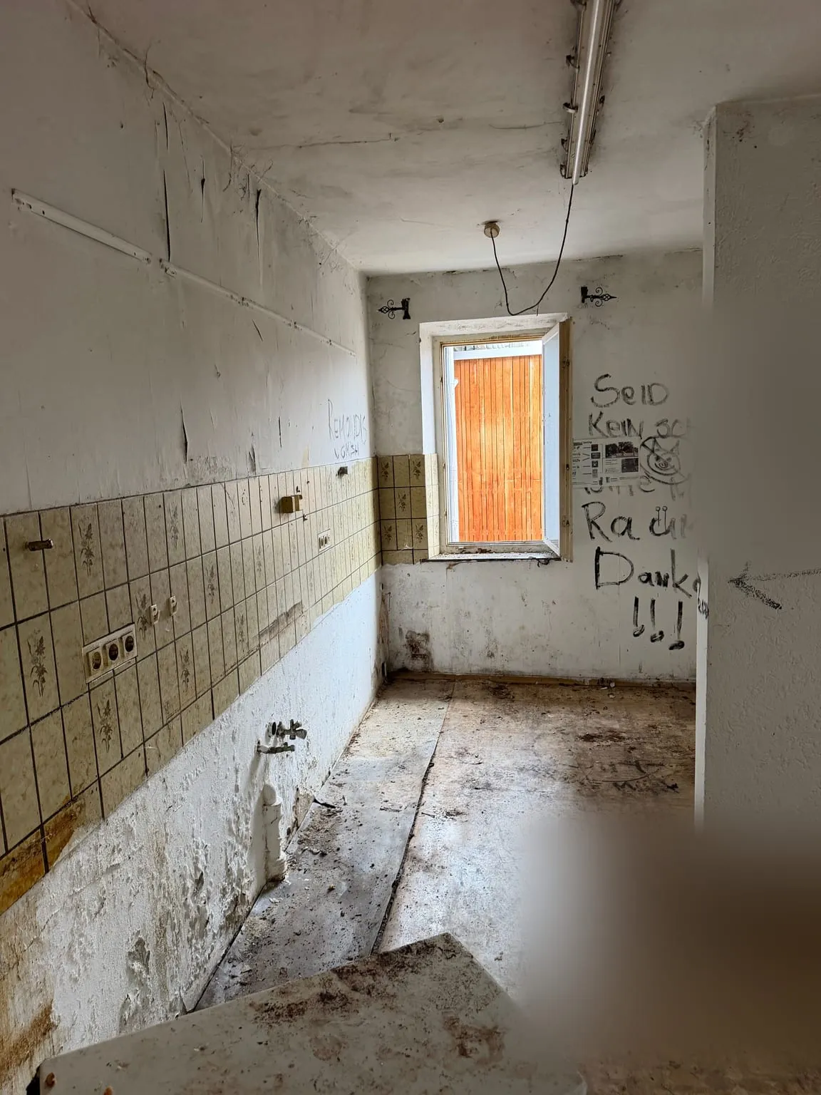 Dieselbe Küche geräumt, mit freiem Boden, Fliesenspiegel an der linken Wand und Fenster an der Stirnseite.