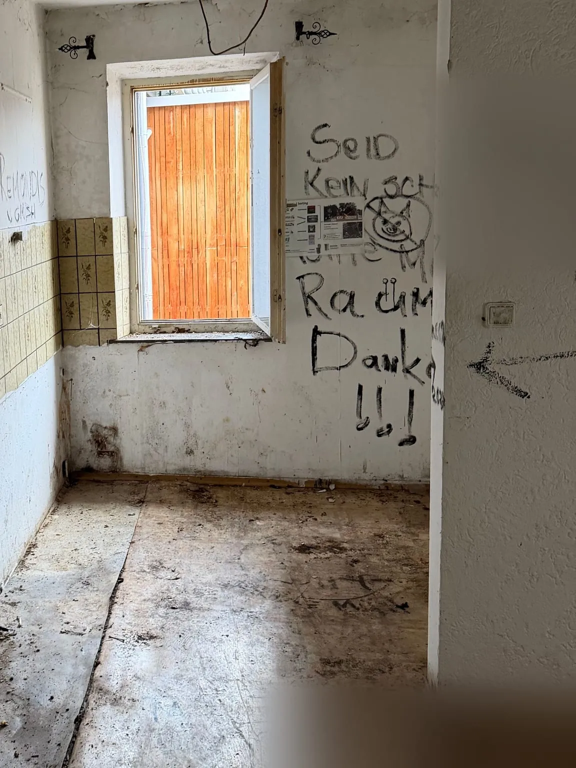 Dieselbe Küchenecke nach der Räumung: Unter dem Fenster mit beschrifteter Wand und Fliesenreihe ist der Boden leer.