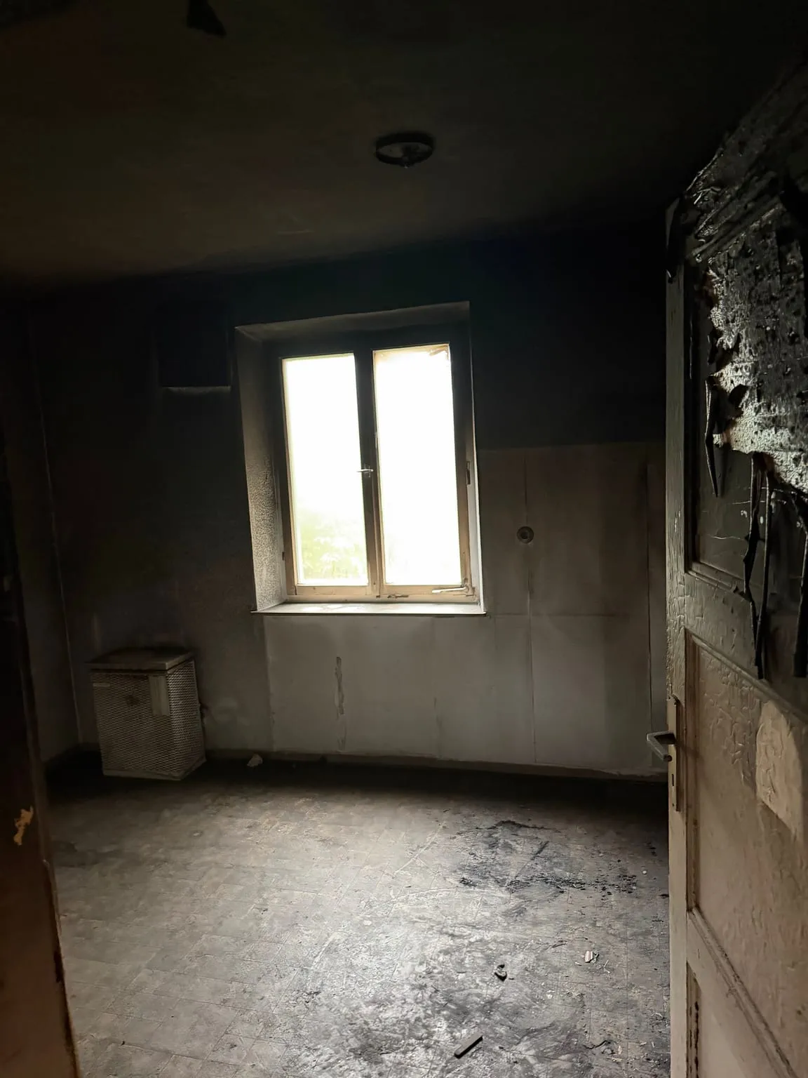 Dasselbe verrußte Zimmer leer geräumt, nur der kleine Gitterkasten steht noch links an der Wand unter dem Fenster.