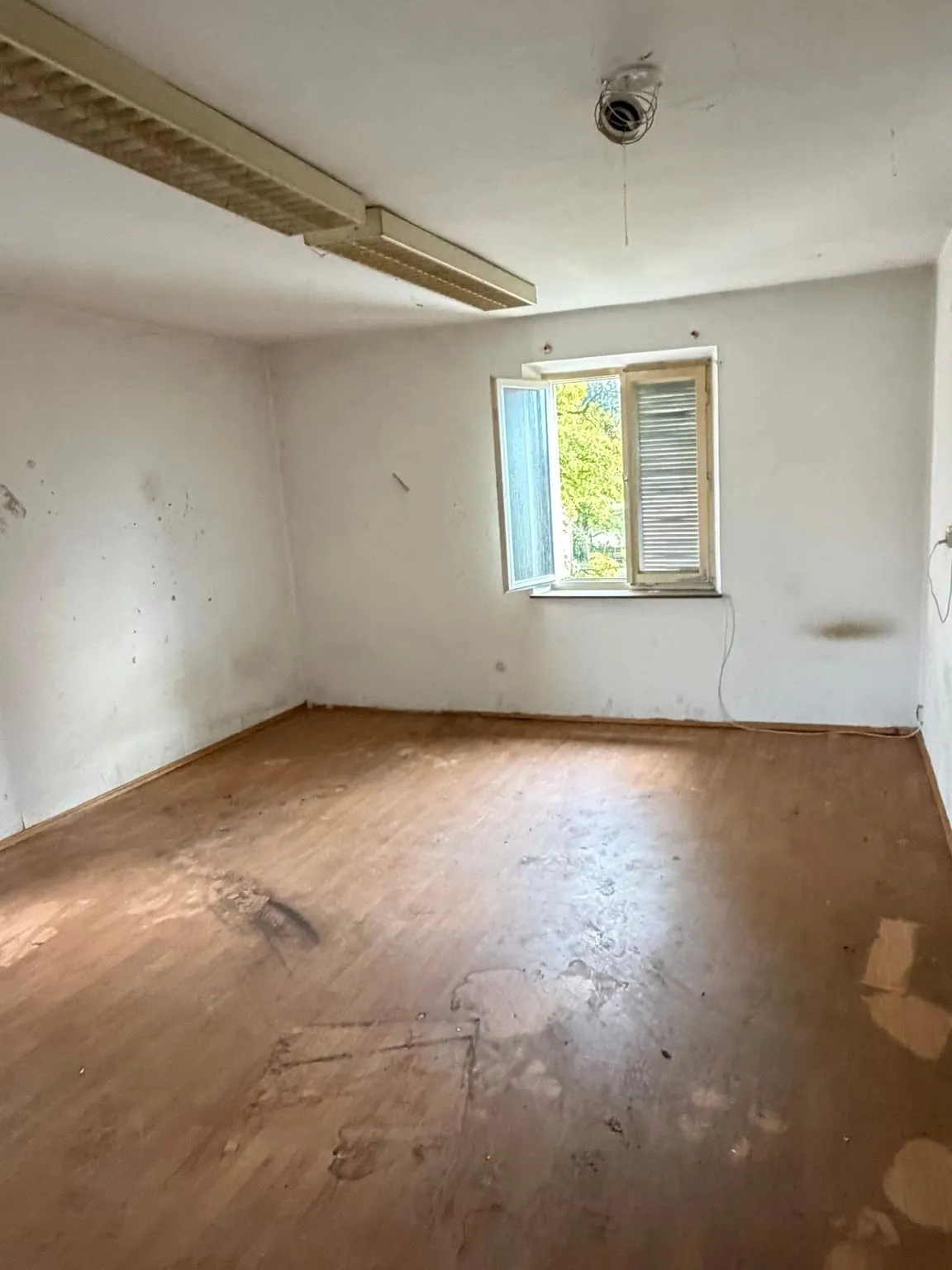 Dasselbe Zimmer nach der Räumung: leerer Laminatboden mit hellen Stellflecken, Fensterwand mit geöffnetem Fenster