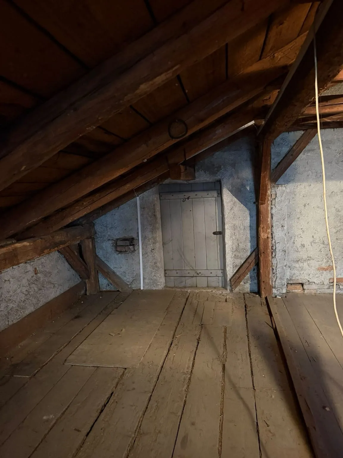 Dieselbe Wand mit der Brettertür nach der Räumung, rechts nur noch ein Holzpfosten vor dem Mauerwerk, davor freier Dielenboden