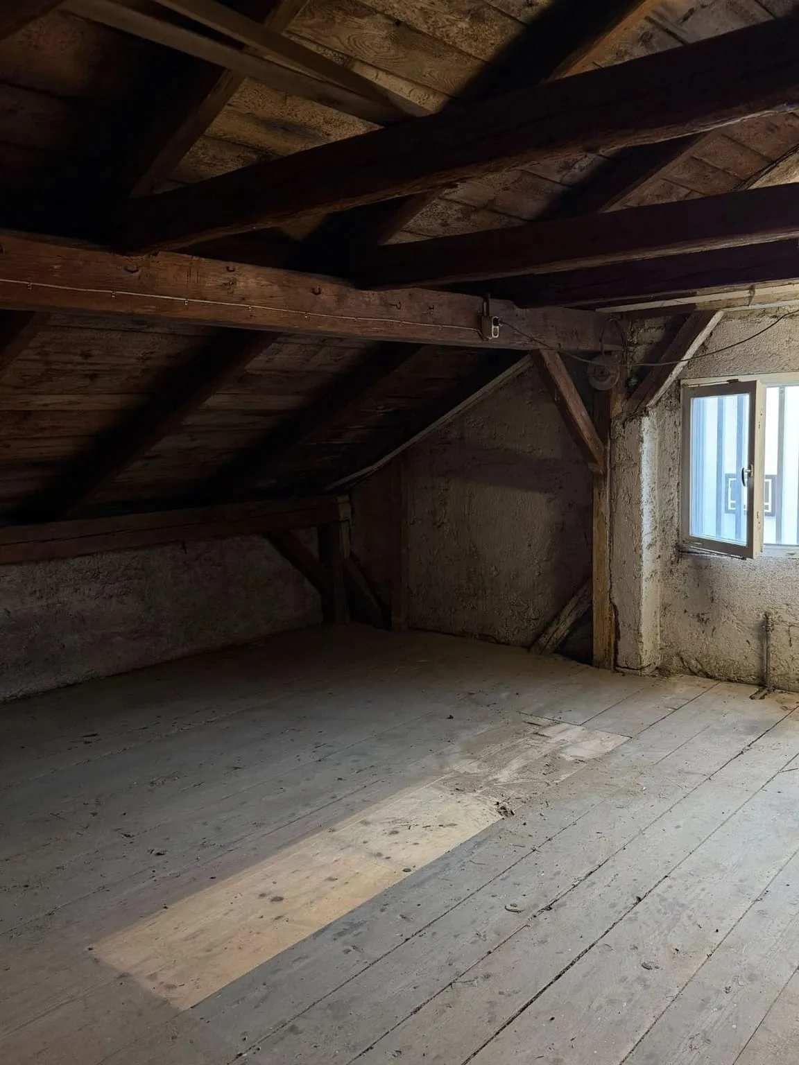 Derselbe Dachboden leer, Sonnenlicht auf den Dielen, hinten die Wand mit dem Fenster unter dem Dachbalken