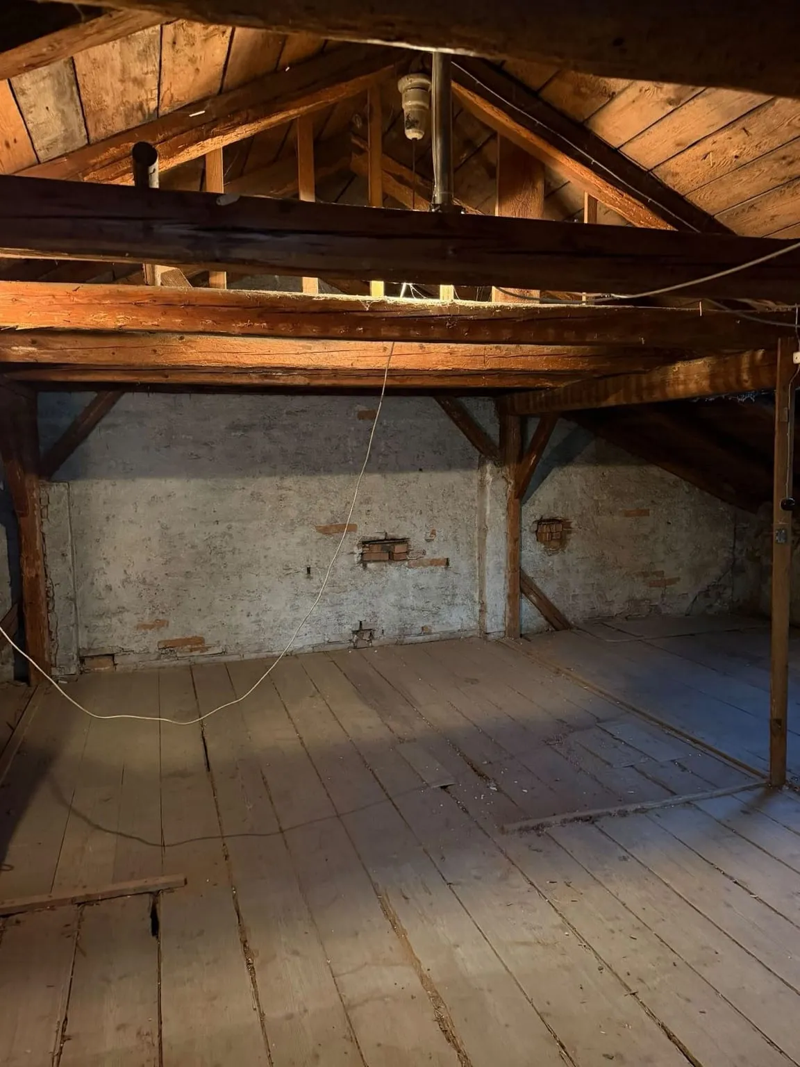 Dieselbe Stelle ohne Schrank und Lattenverschlag: gemauerte Wand unter den Dachbalken, rechts ein Holzpfosten, davor blanker Dielenboden
