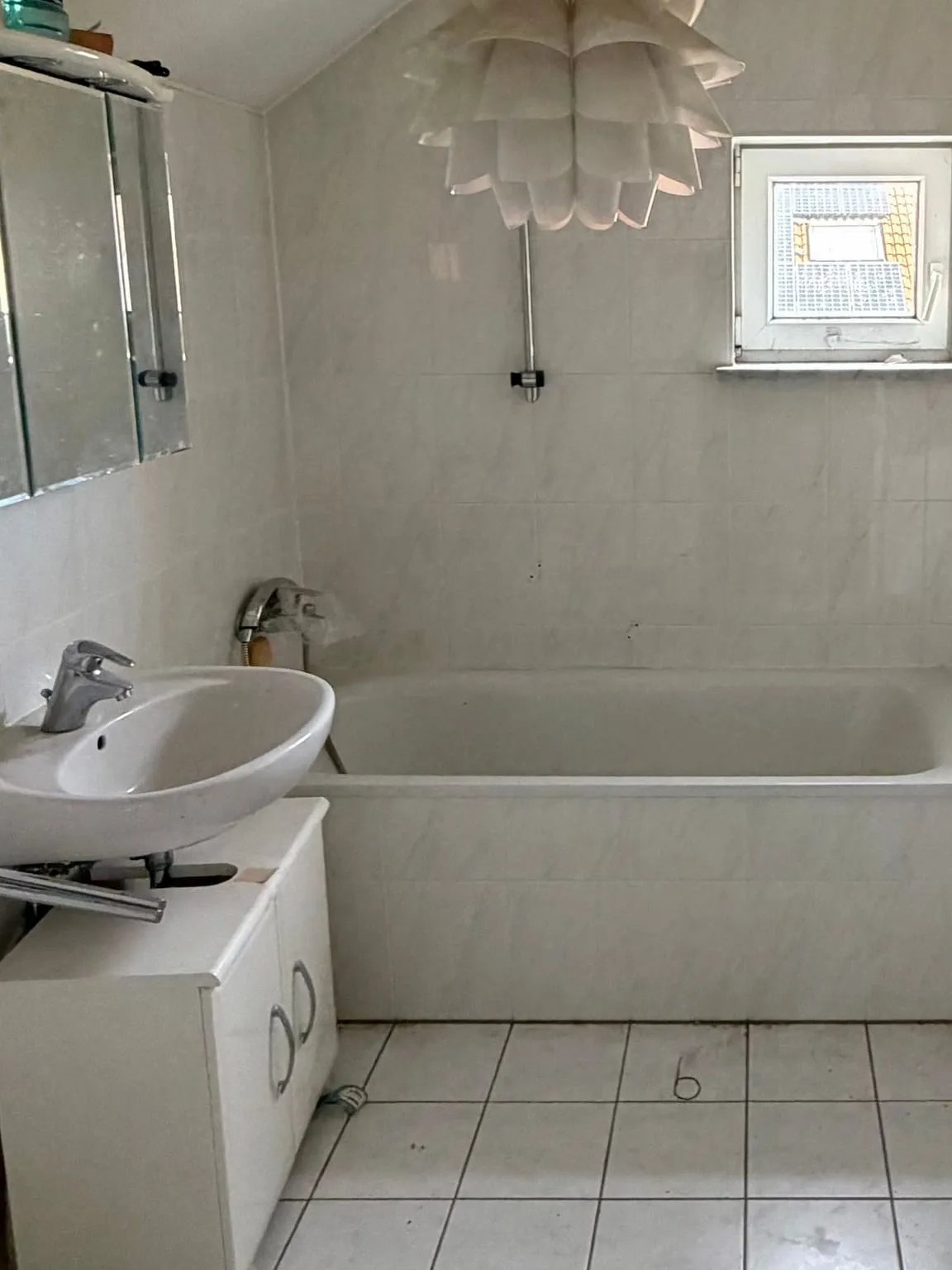 Dasselbe Bad nach der Räumung: leere Badewanne unter dem kleinen Fenster, links Waschbecken und Spiegelschrank, die gefliesten Wände frei.