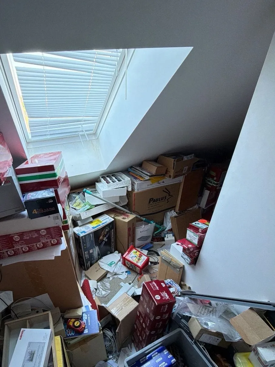 Dachgeschossraum mit Dachfenster, darunter bis zur Fensterbank gestapelte Kartons, Kisten und Folien.