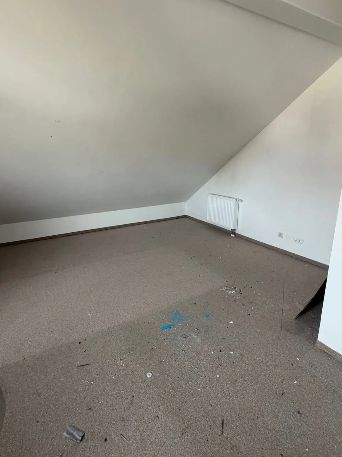 Dieselbe Ecke des Dachgeschossraums leer geräumt, mit grauem Teppich, Dachschräge und Heizkörper an der Giebelwand.