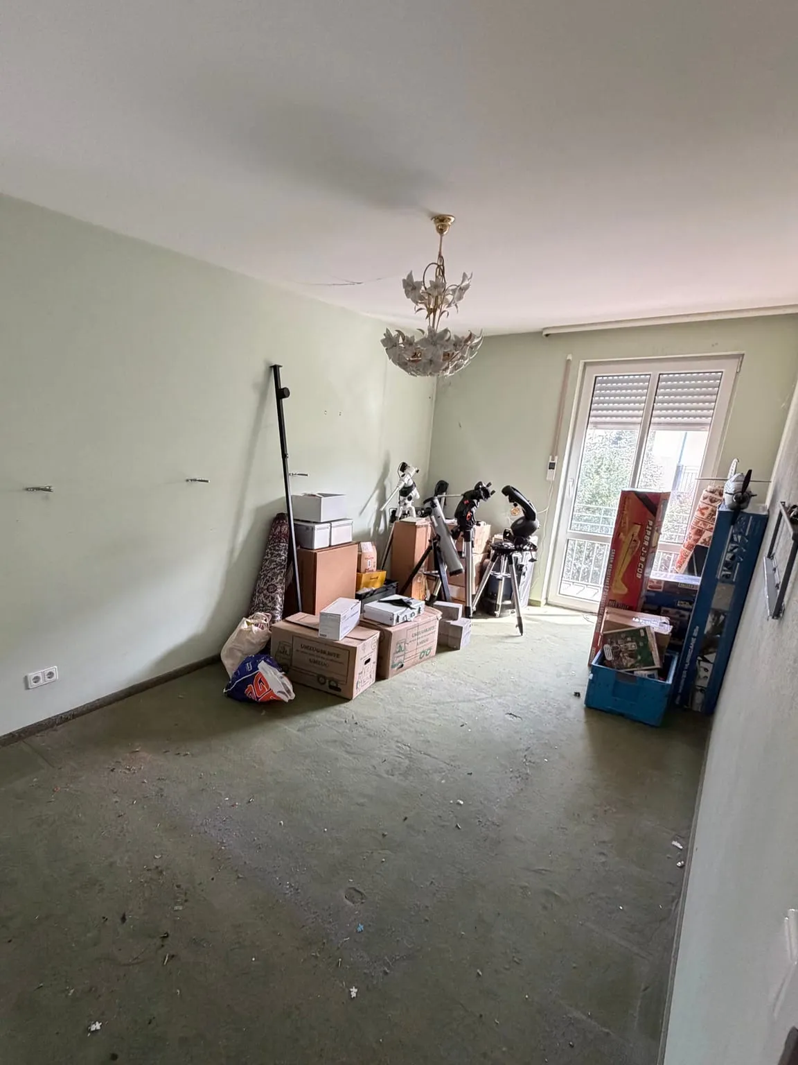 Dasselbe Zimmer nach der Räumung mit freiem Teppichboden, vor der Balkontür stehen noch einige Kartons und Teleskope.