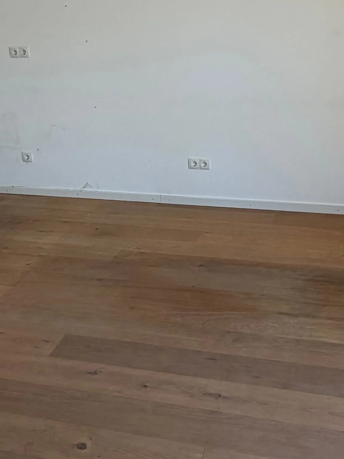 Leere weiße Wand mit Doppelsteckdose über einem freien Holzdielenboden