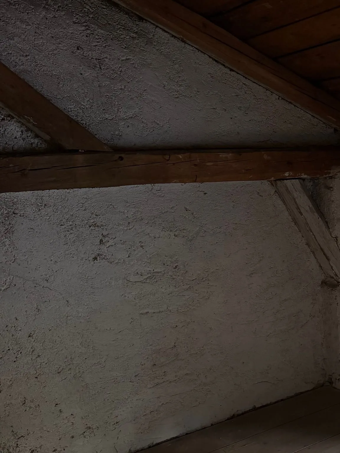 Dieselbe Wand nach der Räumung: leere, verputzte Wand unter dem Dachbalken mit hellem Kopfband und Holzdielen am Boden