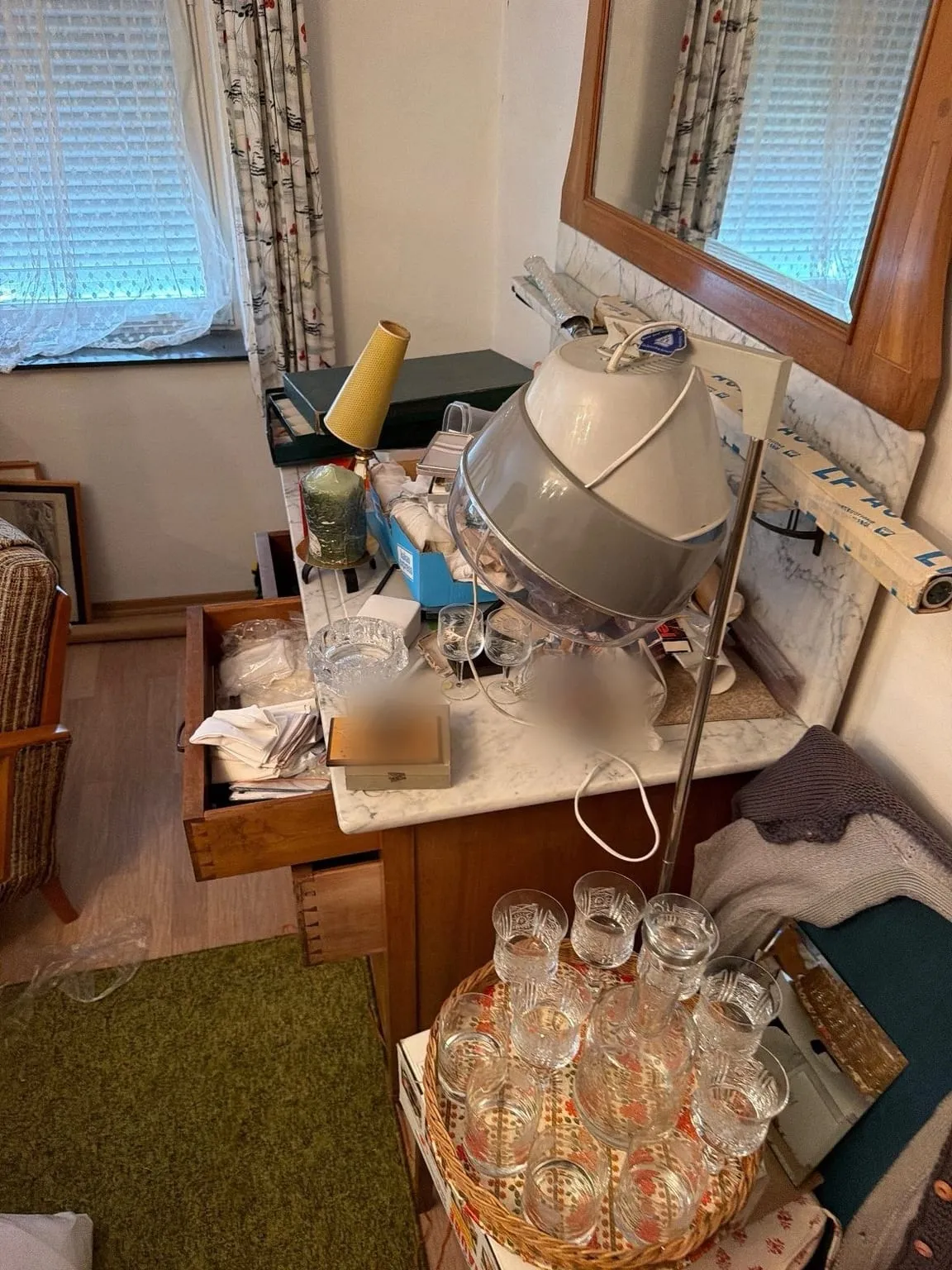 Schlafzimmerecke am Fenster mit Marmorkommode, Spiegel, Trockenhaube, Lampe und einem Tablett mit Gläsern