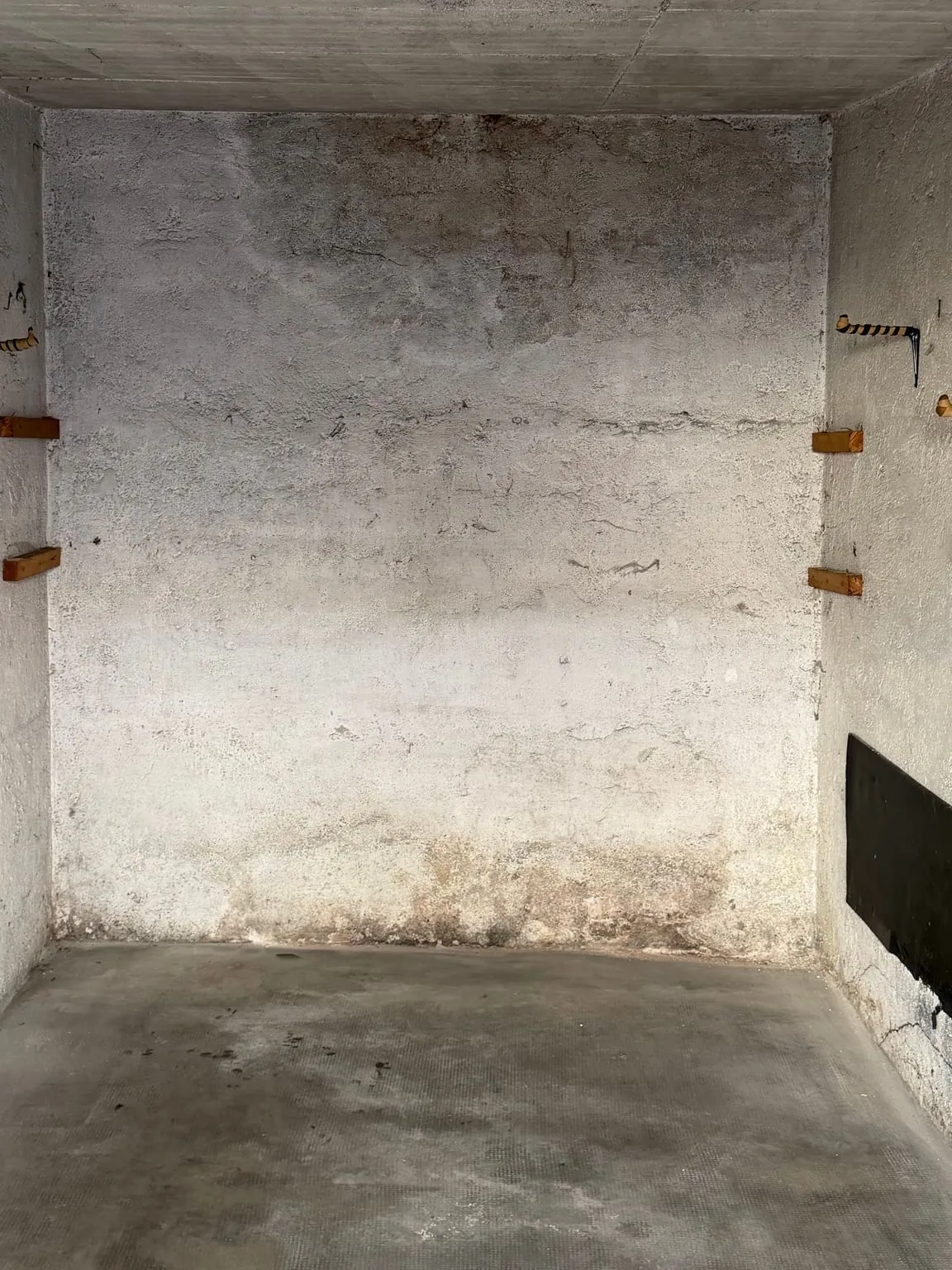 Dieselbe Garage leer, mit kahler Betonrückwand, Holzauflagen an den Seitenwänden und einer schwarzen Schutzmatte rechts