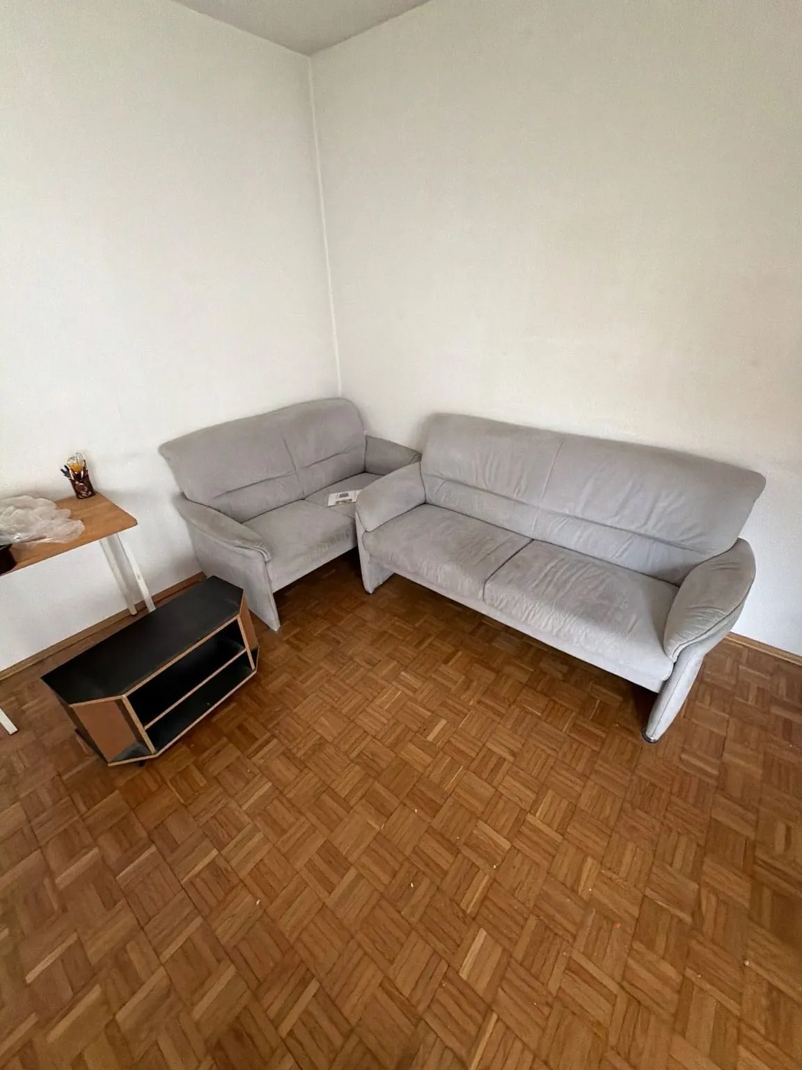 Zimmerecke mit zwei hellgrauen Sofas, einem kleinen Holztisch und einem schwarzen Fernsehmöbel auf Parkettboden