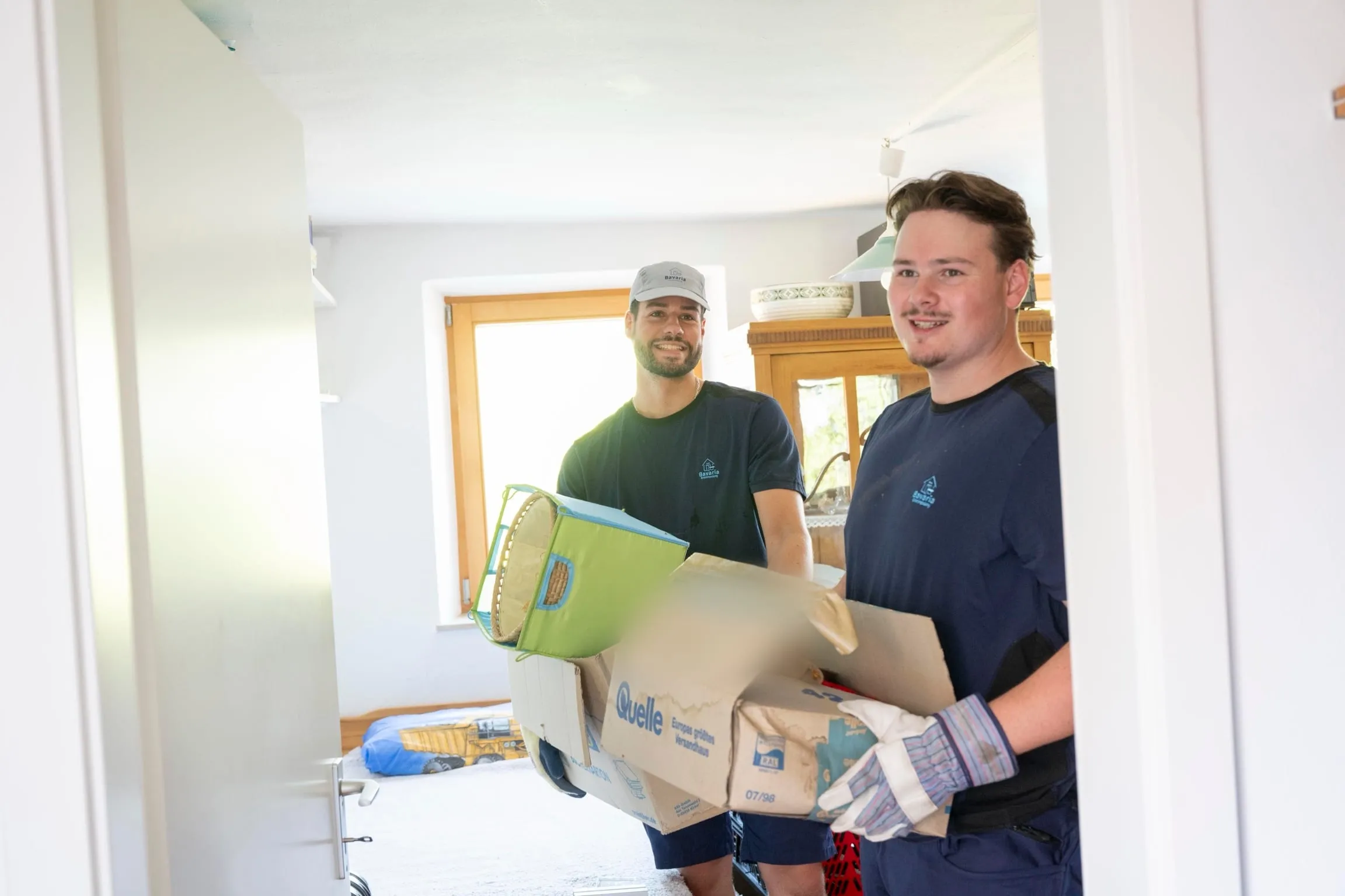 Zwei Mitarbeiter tragen gepackte Kartons durch eine Wohnung